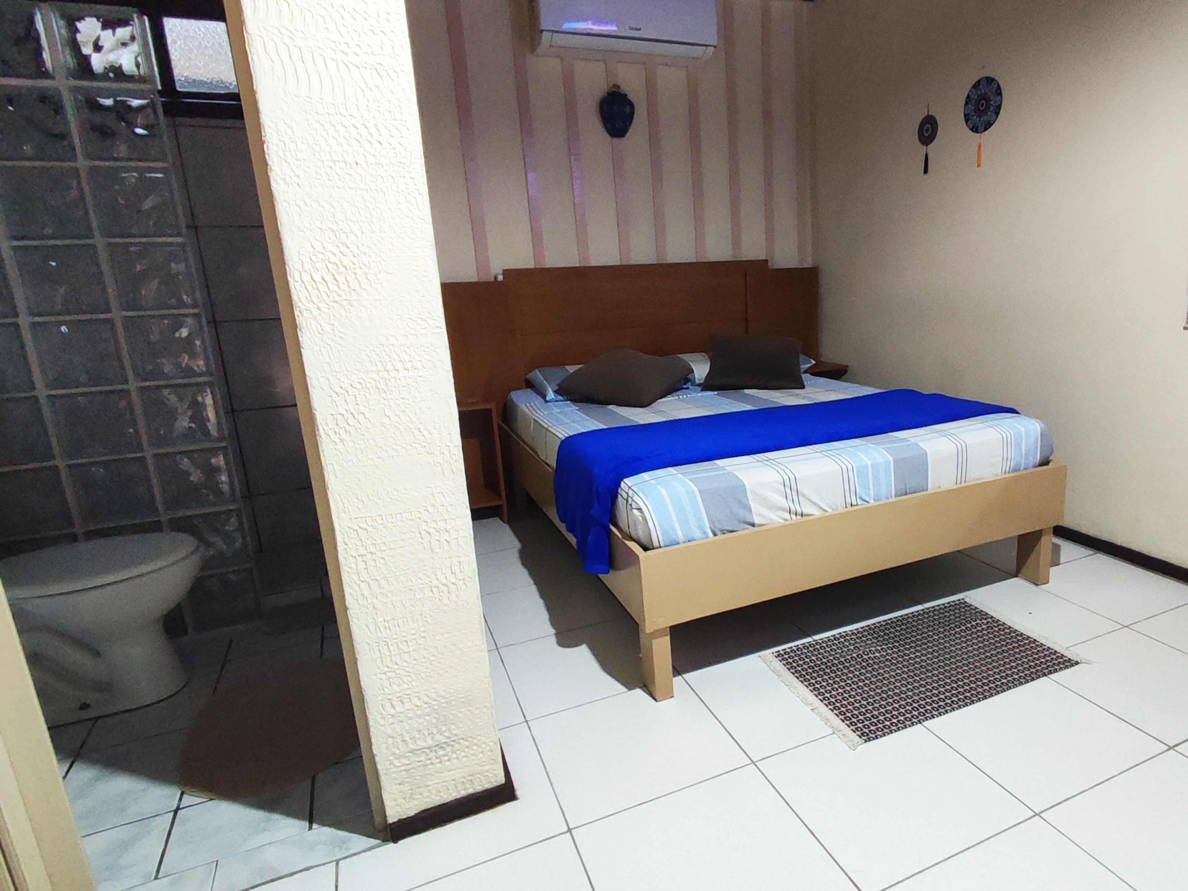 A bedroom with a bed, a nightstand, a wall-mounted air conditioner, and a bathroom with a toilet and shower.