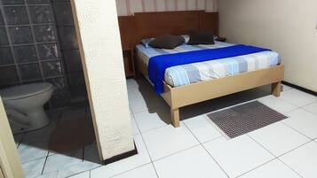 A bedroom with a bed, a nightstand, a wall-mounted air conditioner, and a bathroom with a toilet and shower.