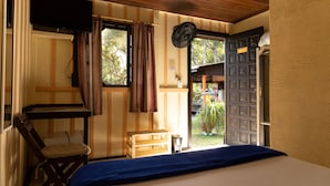 Una habitación con cama, escritorio, silla, ventana con cortinas y puerta que da al exterior.