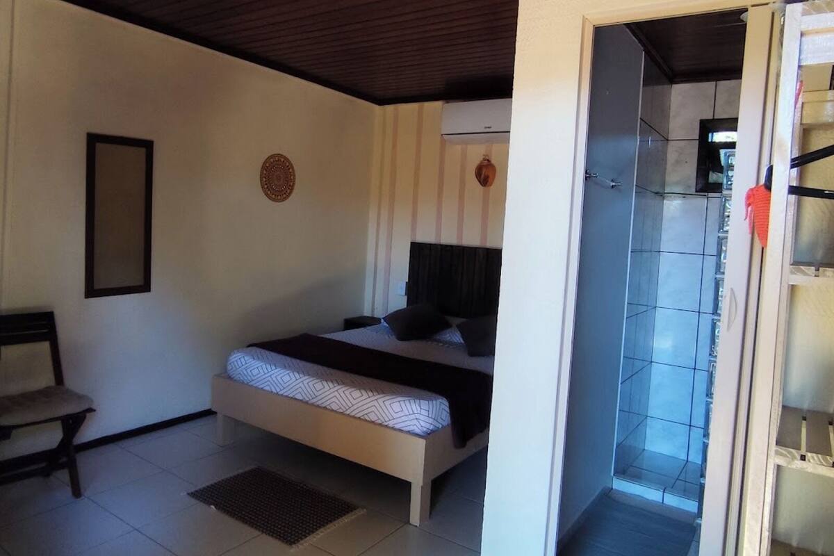 A bedroom with a bed, a chair, a wall decoration, and a bathroom visible through an open door.