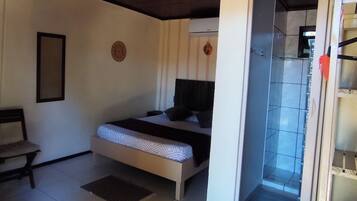 Quarto com cama, poltrona, decoração na parede e banheiro visível por uma porta aberta.