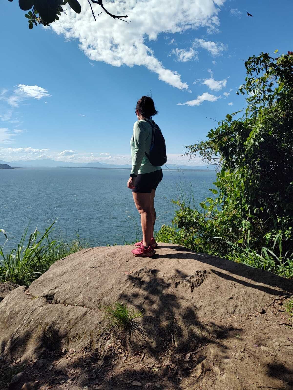 Une personne se tient sur un rocher, surplombant une étendue d’eau, avec des montagnes à l’horizon.