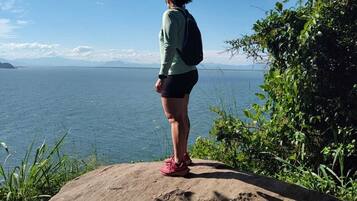 Une personne se tient sur un rocher, surplombant une étendue d’eau, avec des montagnes à l’horizon.