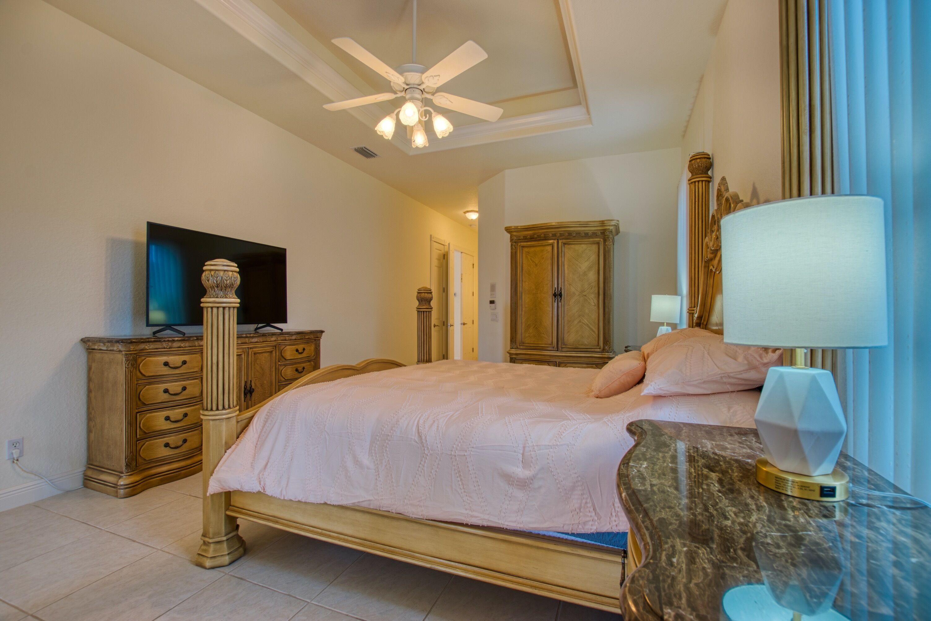 A bedroom with a bed, a television, a cabinet, a lamp, and a ceiling fan.
