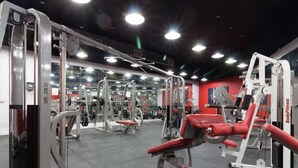A gym with various exercise machines, mirrors, and red walls.