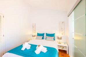 A hotel room with a bed, two pillows, a nightstand with a lamp, and towels.