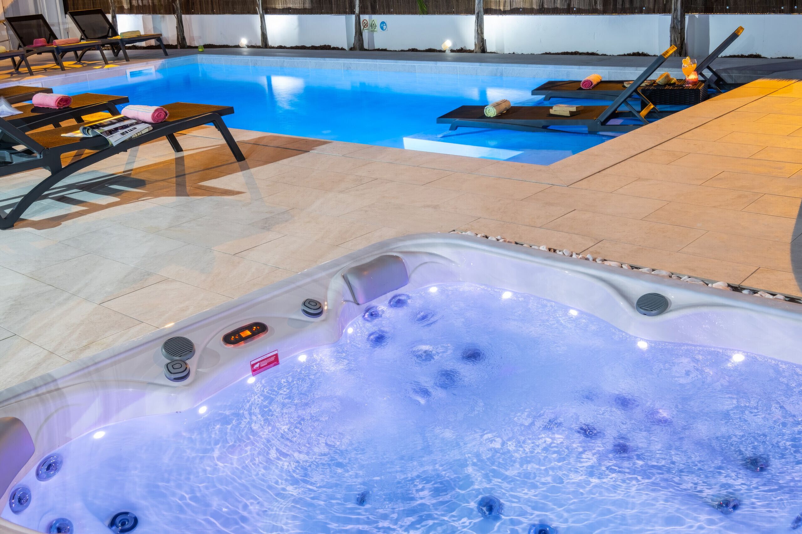 Un espace piscine comprenant des chaises longues, un jacuzzi et une terrasse carrelée.