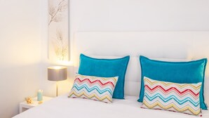 Uma cama com duas almofadas, uma mesa de cabeceira com abajur e uma obra de arte pendurada na parede.