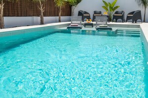 A clear blue pool with lounge chairs and a table, surrounded by a low wall and plants. - Modern villa w/ heatable pool & BBQ, Albufeira (Albufeira)