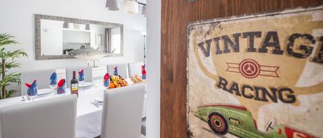 A dining area with a white table set for four, a large mirror above the table, and a wall with a vintage racing sign.