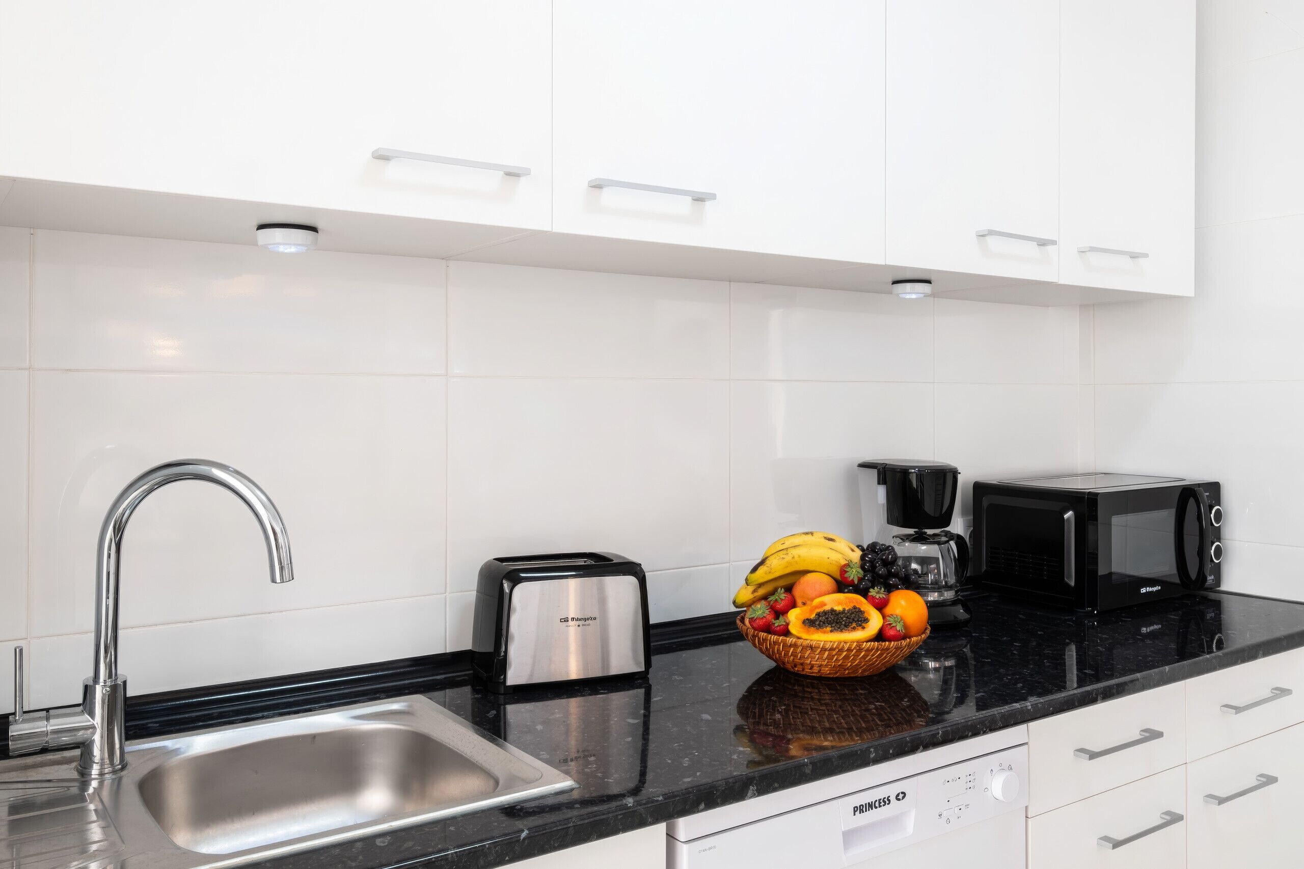 Een moderne keuken met een roestvrijstalen spoelbak, een broodrooster, een koffiezetapparaat, een magnetron en een fruitschaal op het aanrecht.