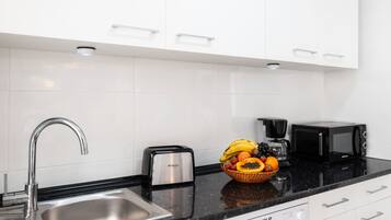 Een moderne keuken met een roestvrijstalen spoelbak, een broodrooster, een koffiezetapparaat, een magnetron en een fruitschaal op het aanrecht.