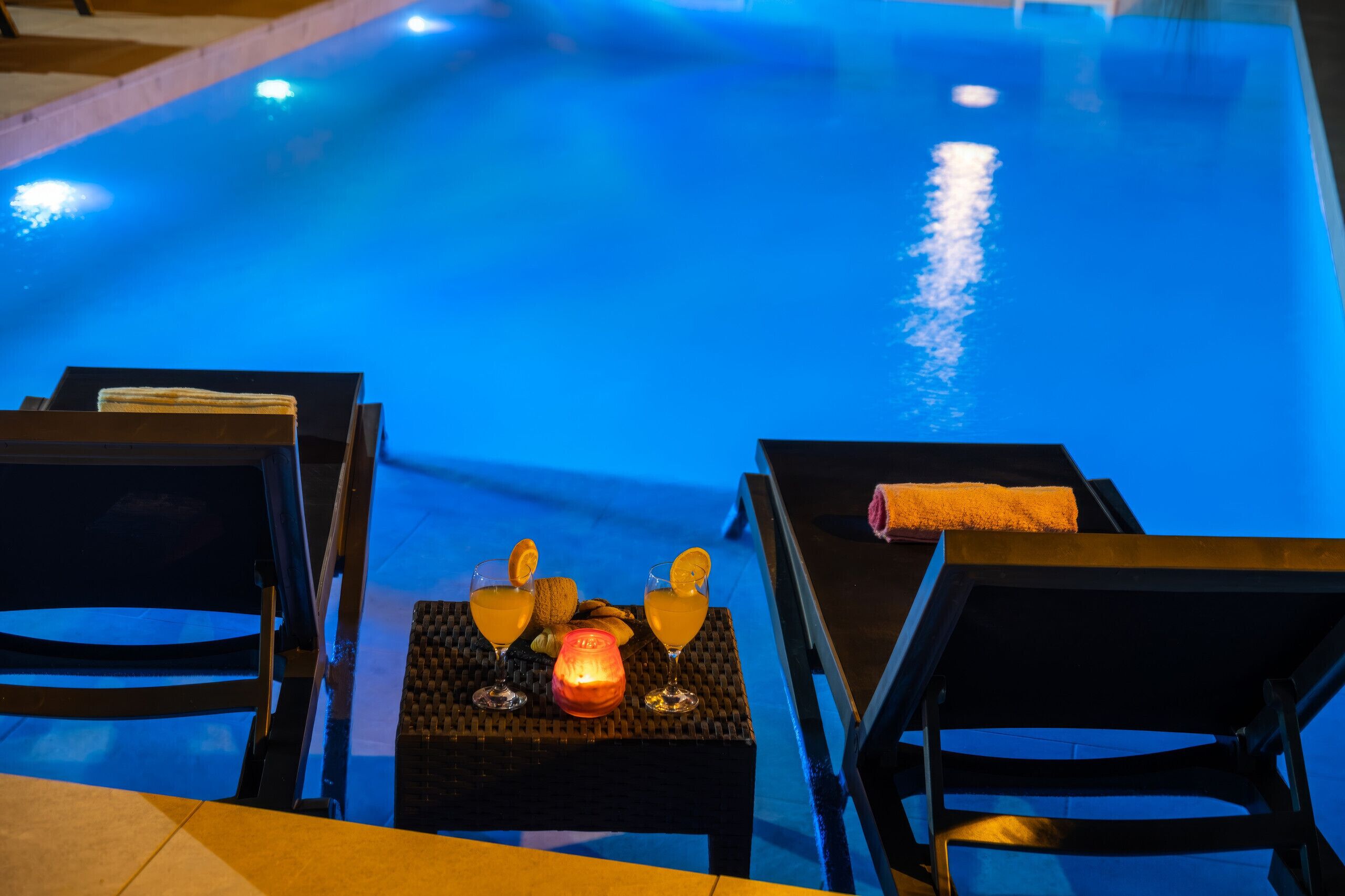 A poolside area with lounge chairs and a table with a candle and snacks.