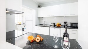 Eine moderne Küche mit weißen Schränken, einer schwarzen Arbeitsplatte, einem Geschirrspüler, einer Kaffeemaschine und einer Weinflasche.
