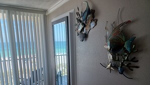 A room with a view of the ocean through a sliding door, a decorative fish sculpture on the wall, and a wooden floor.