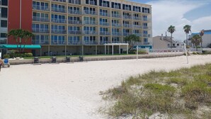 A multi-story hotel with balconies, a beach in the foreground, and palm trees.