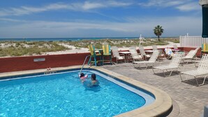 A pool area with a view of the beach, lounge chairs, and a sign indicating 'Room Guests Only'.