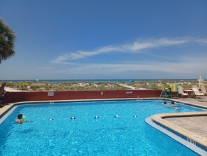 Una piscina con agua azul cristalina, rodeada de sillones de descanso y vista a la playa.