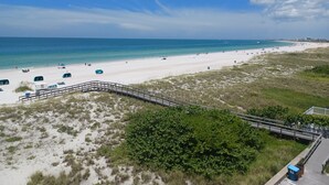 A beach with a wooden walkway, white sand, and a view of the ocean.