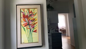Un cuadro enmarco con flores en una pared de una habitación con suelo de madera y paredes blancas.