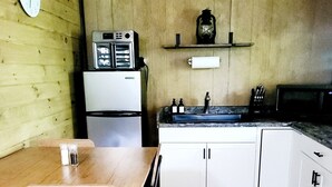 A compact kitchen with wooden walls, a refrigerator, a microwave, a sink, and a clock on the wall. - Rustic Private Cabin on 30 acres w/Loft/Firepit/Secluded/Trails (Patriot)