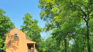A cozy outdoor seating area with Adirondack chairs around a fire pit, a wooden deck, and a large house in the background. - Rustic Private Cabin on 30 acres w/Loft/Firepit/Secluded/Trails (Patriot)