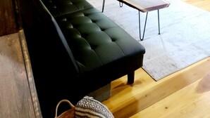 A room with a black sofa, a small table with a candle, and a wooden floor. - Rustic Private Cabin on 30 acres w/Loft/Firepit/Secluded/Trails (Patriot)