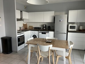 Une cuisine moderne avec des meubles blancs, un lave-linge, un réfrigérateur et un four à micro-ondes.