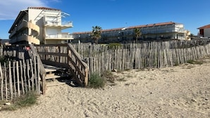 Una proprietà fronte spiaggia con un recinto in legno, una scala che conduce a un balcone e un edificio con tetto in tegole rosse.