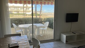 Una stanza con una porta scorrevole in vetro che dà su uno spazio esterno con tavolo e sedie, una TV montata a parete e un piccolo armadietto bianco.