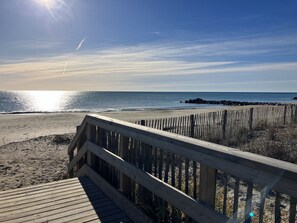 A wooden boardwalk leading to a sandy beach with a rocky outcrop in the distance.