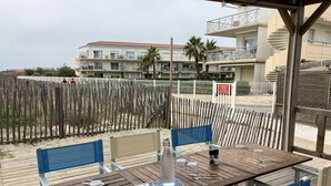 Un pontile in legno con un tavolo apparecchiato per due, con vista su una spiaggia sabbiosa e una fila di edifici con balconi.