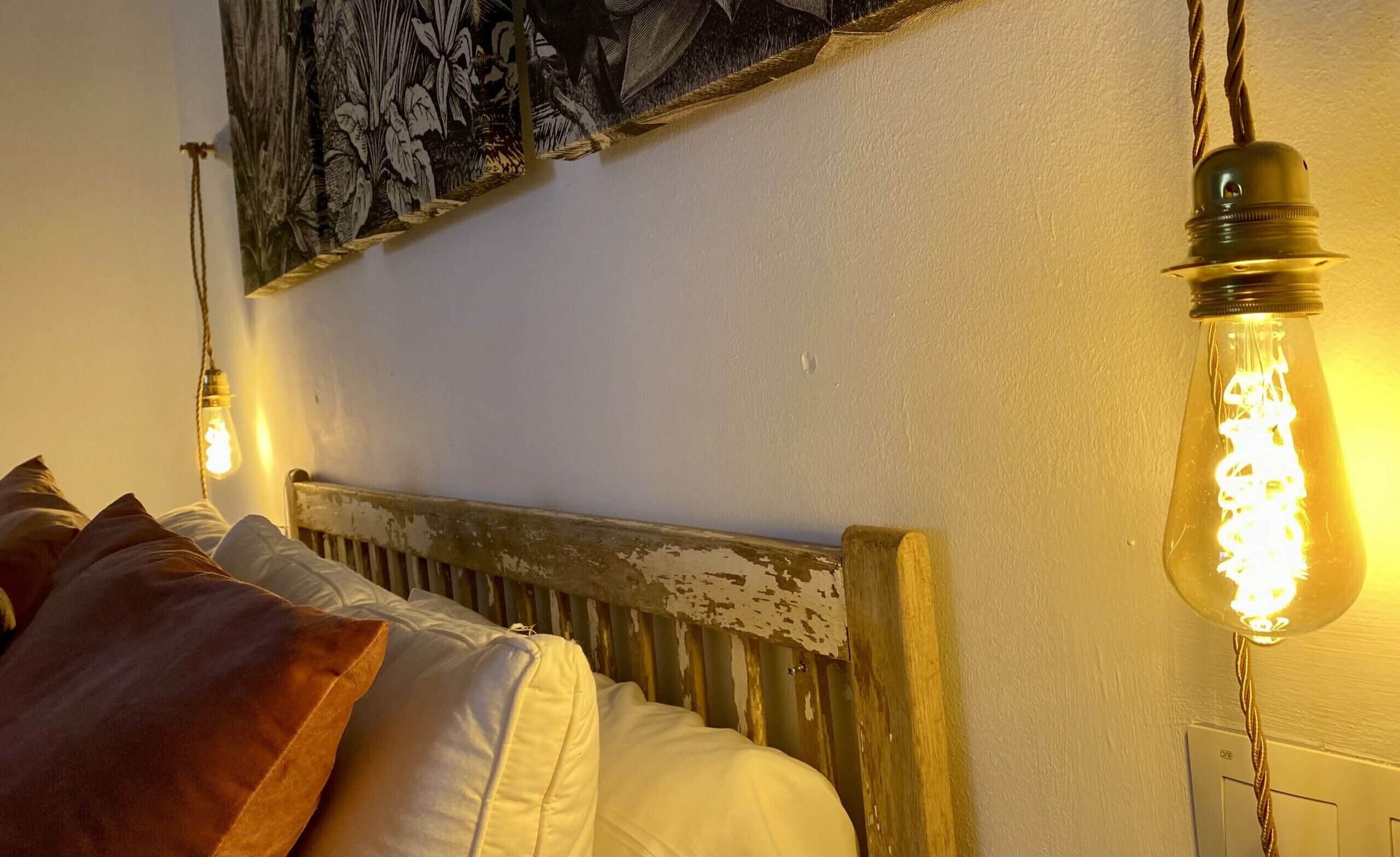 Una cama con cabecera rústica, una pared con tapiz floral y una bombilla colgante.