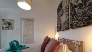 Une chambre à coucher avec une couvre-lit à motifs, une tête de lit en bois et une grande estampe représentant des plantes accrochée au mur.