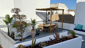 Une terrasse sur le toit, avec une table et des chaises en bois, entourée de plantes en pot et agrémentée d’une pergola.