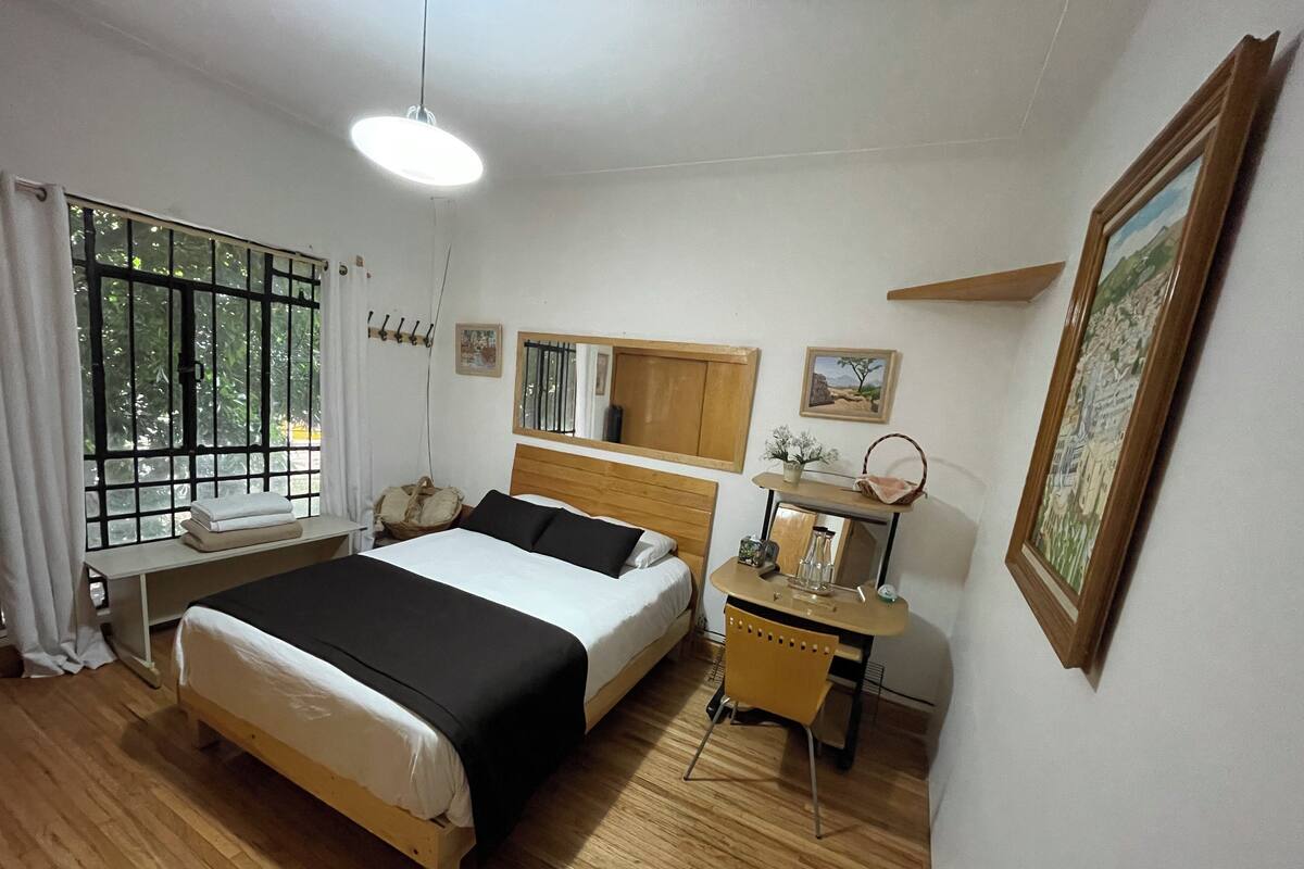 A bedroom with a bed, bedside table, mirror, and a window with curtains.