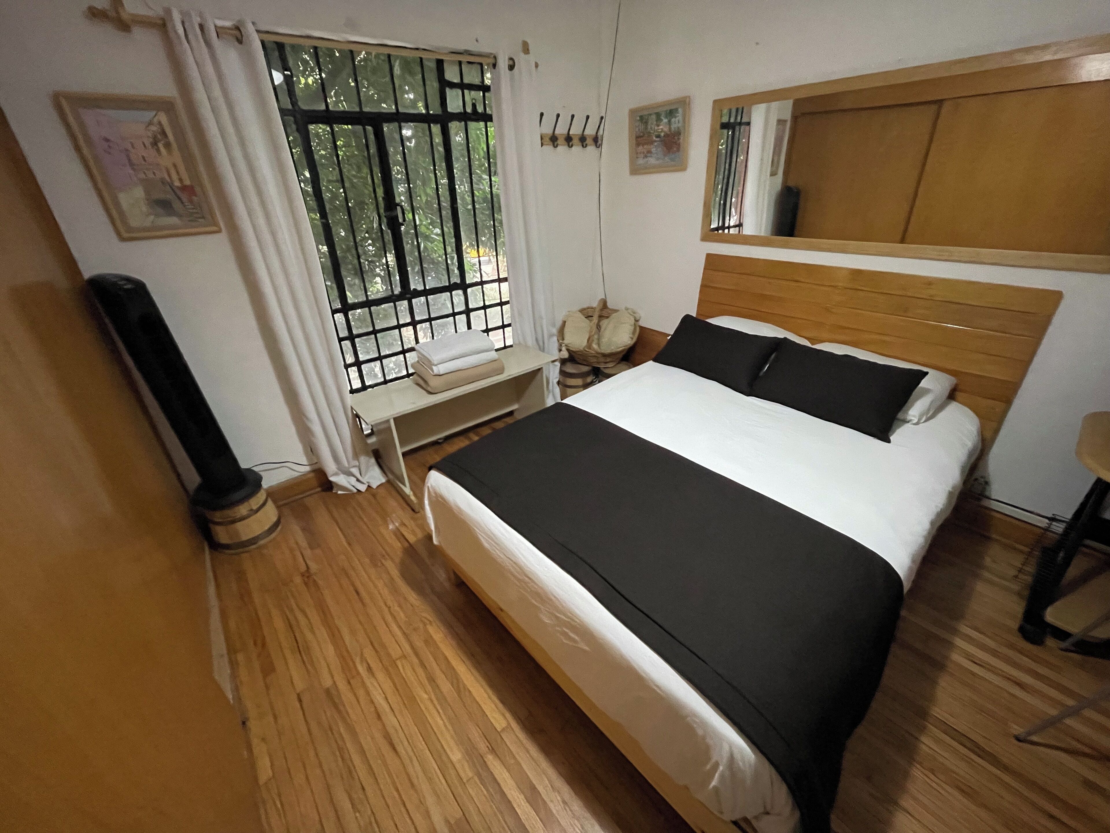A bedroom with a wooden bed, a window with bars, a bedside table with a lamp, and a wooden headboard.