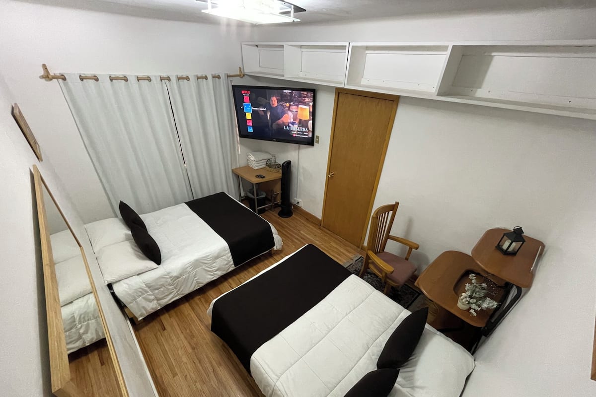 A compact hotel room with two beds, a TV, a small table, and a chair.