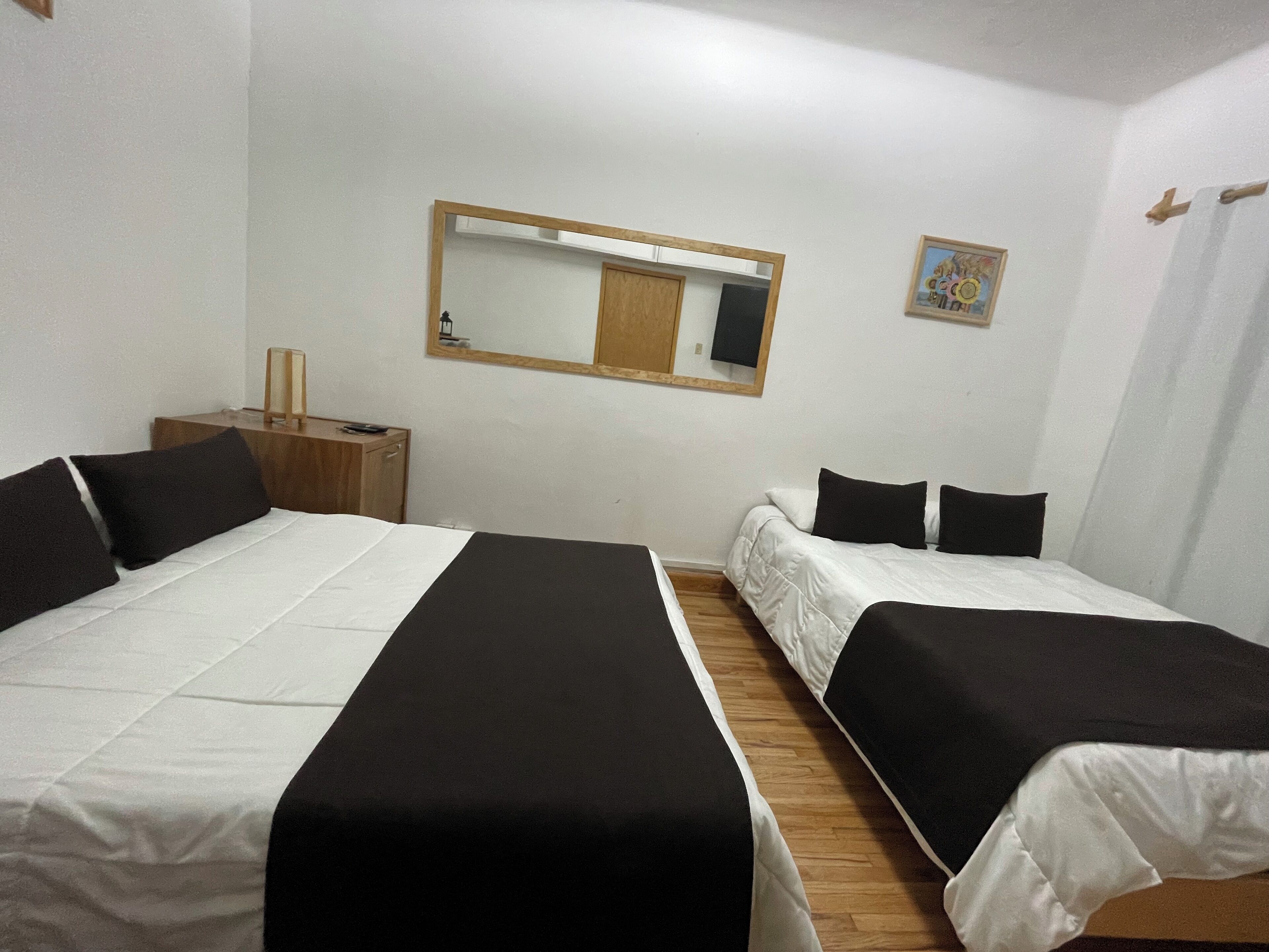 A room with two beds, a wooden nightstand, a mirror, and a small painting on the wall.