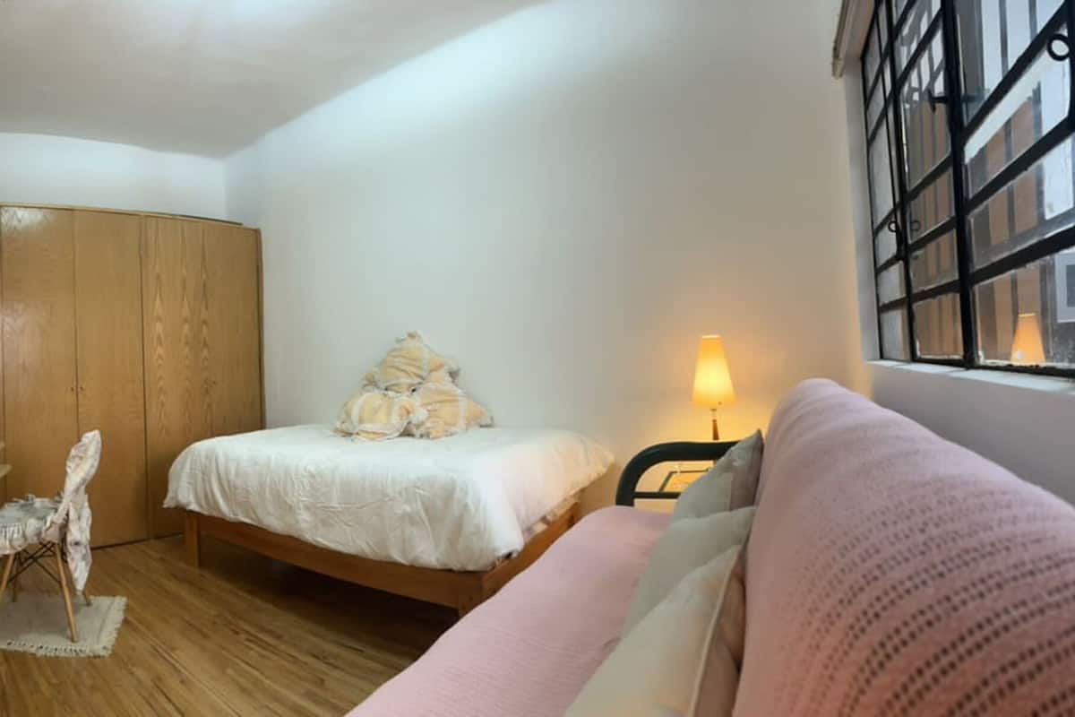 A bedroom with a bed, a chair, a small table, a window with a view, and a wardrobe.