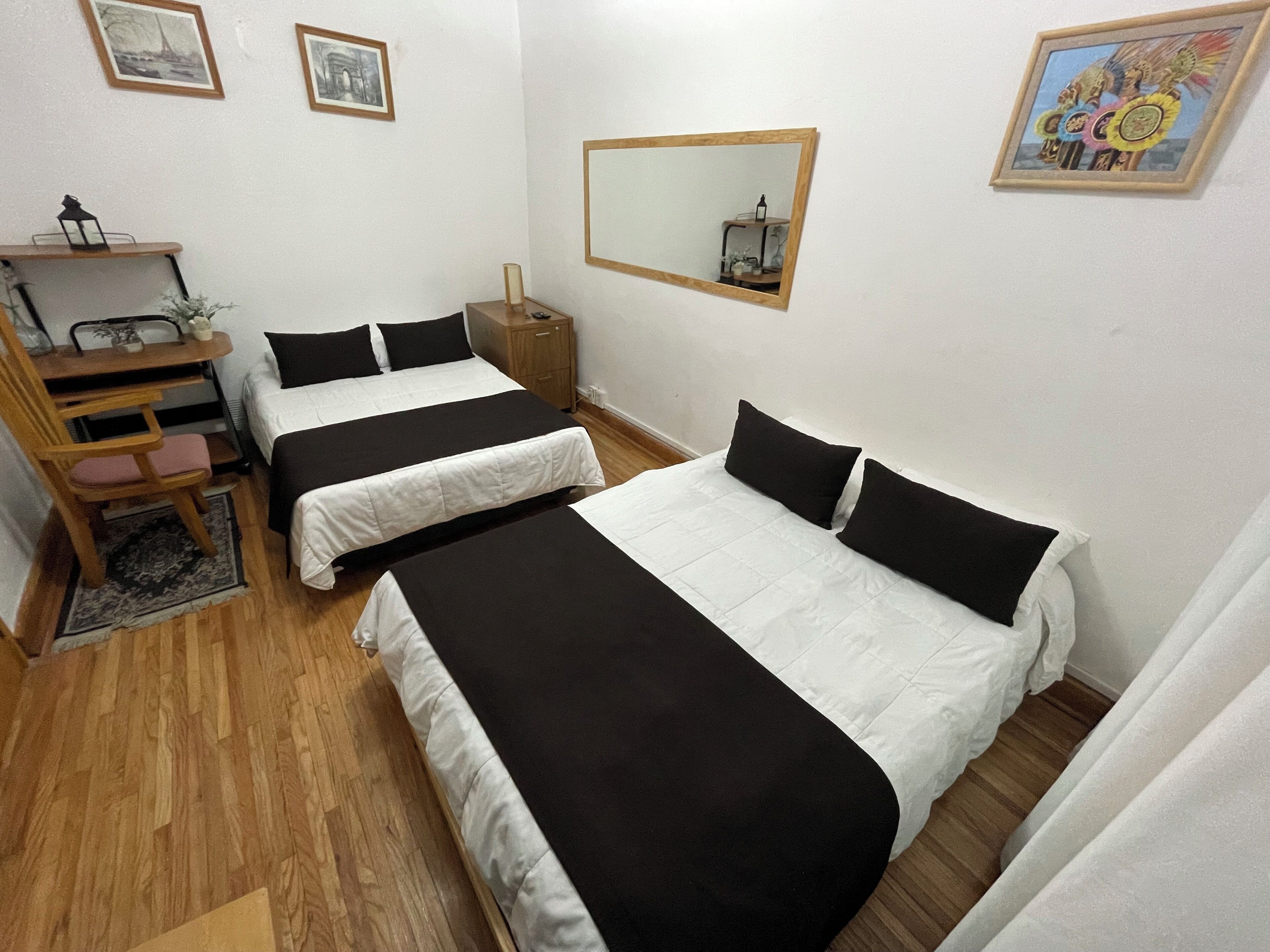 A room with two beds, a desk, a chair, a mirror, and framed pictures on the wall.