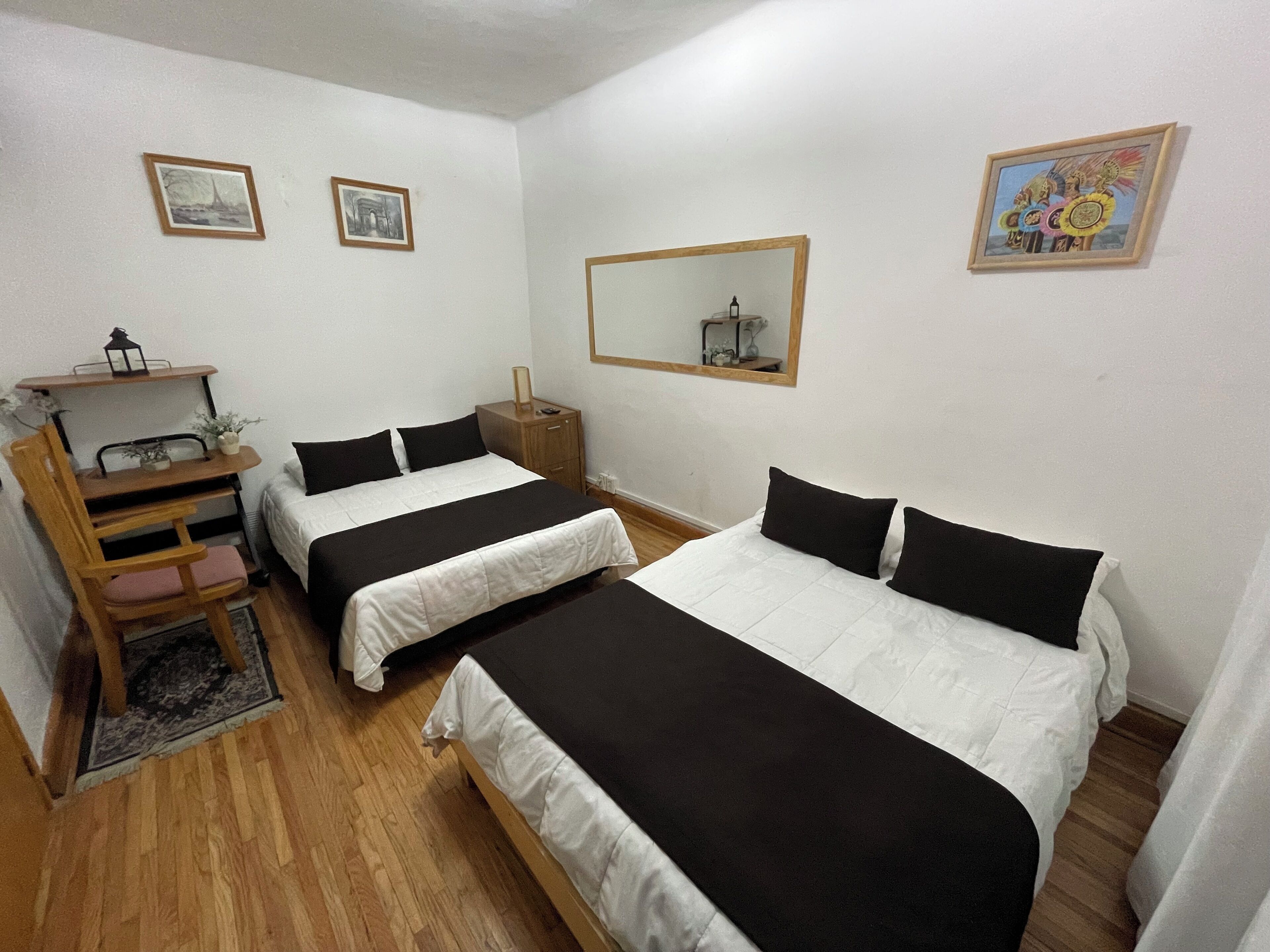 Una habitación con dos camas individuales, un escritorio de madera con una silla, una mesita y un espejo en la pared.