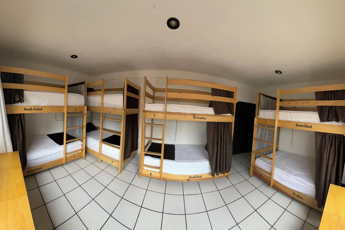 A circular room with bunk beds labeled with names, a bench, and a window.