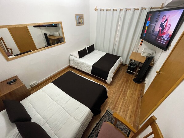 Habitación de hotel con dos camas, televisión, espejo y suelo de madera.