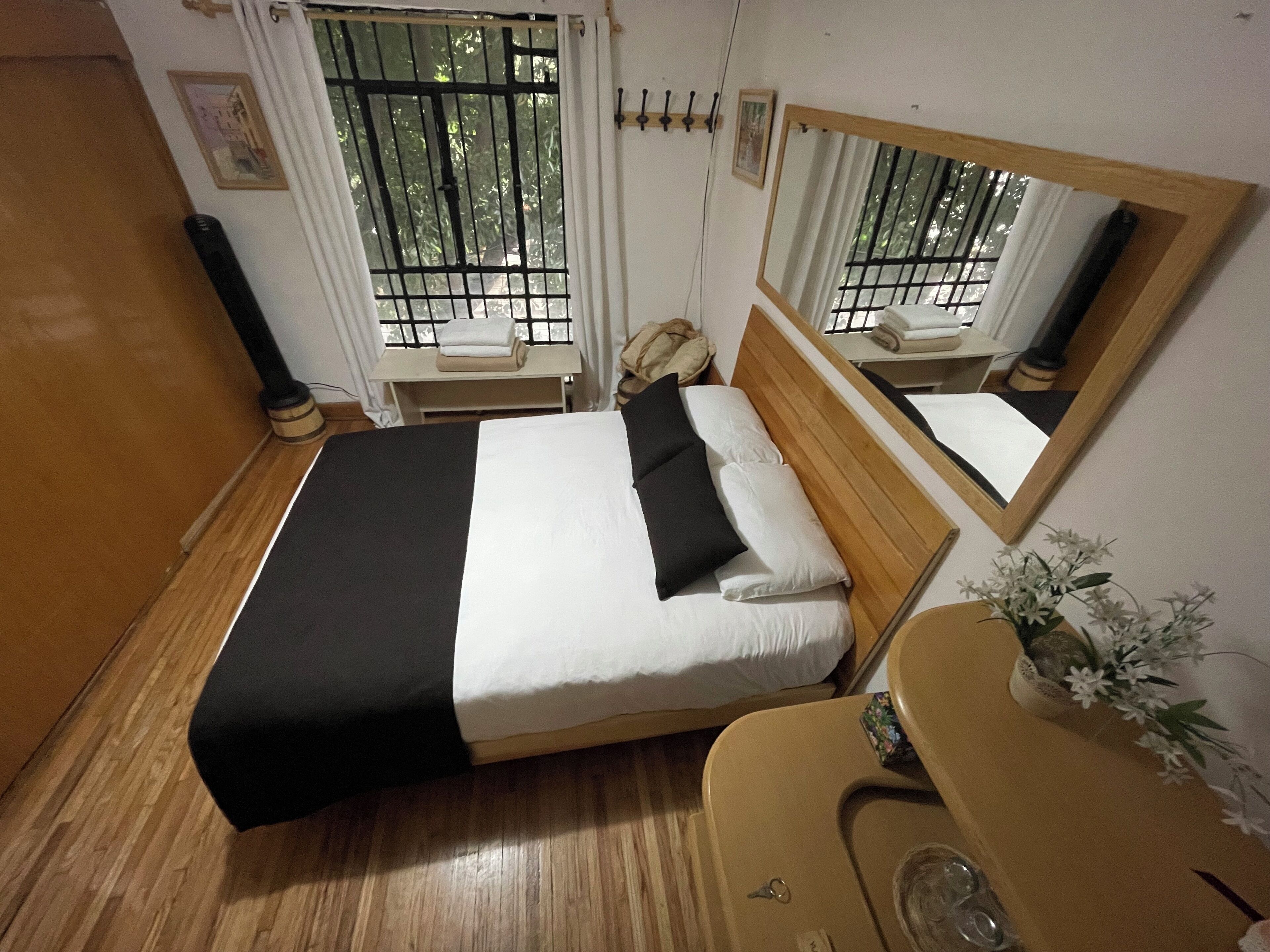 A hotel room with a bed, a wooden headboard, a bedside table, a mirror, and a window with bars.