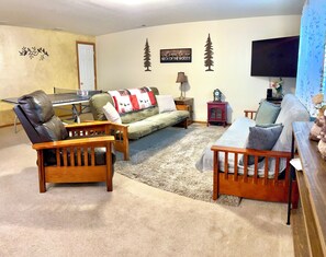 A living room with a sofa, two wooden chairs, a coffee table, a TV, and a wall clock.