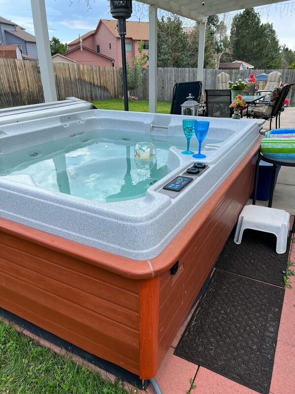 A hot tub with a control panel, two glassware, and a small stool.