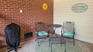 Eine Terrasse mit zwei Metallstühlen, einem kleinen runden Tisch und einer schwarzen Bodenabdeckung.