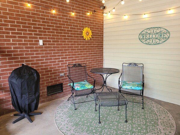 Un patio con dos sillas de metal, una mesita redonda y un cubre suelo negro.