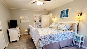 Ein Schlafzimmer mit Bett, Kommode, Fernseher und Deckenventilator.